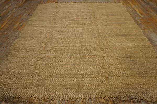 Tan, textured flatweave rug with fringe displayed on rustic light brown wooden floor planks.