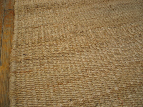 Natural beige rug featuring a heavy looped texture, visible next to wood floorboards.