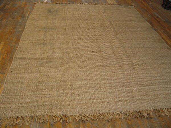 Highly textured light brown flatweave rug with fringe on hardwood flooring.