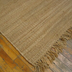 Natural toned, chunky woven rug with thick fringe rests on a distressed golden hardwood floor.