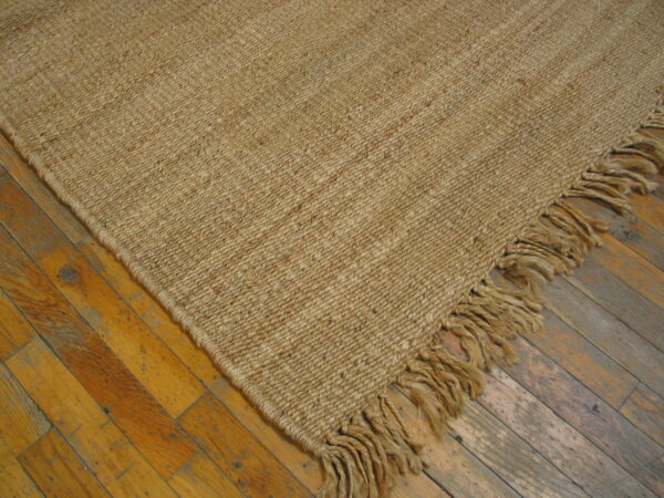 Natural toned, chunky woven rug with thick fringe rests on a distressed golden hardwood floor.