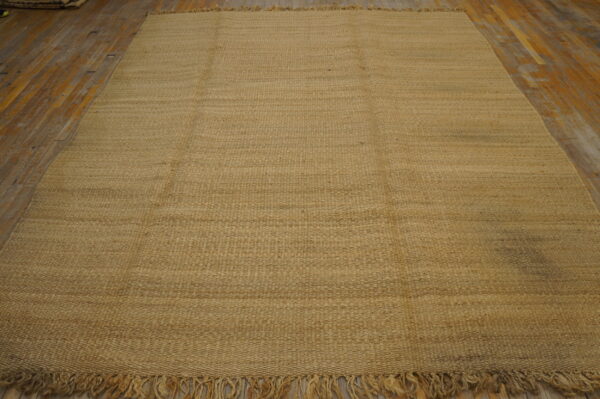 Natural light brown flatweave rug with prominent texture and fringes covers a rustic wood floor.