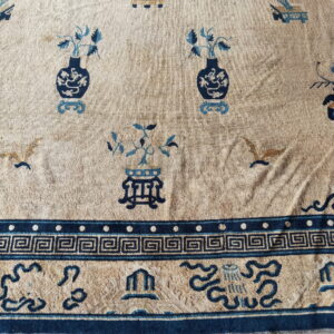 Tan rug with dark and light blue motifs of vases and birds, framed by a Greek key border.