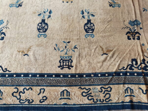 Tan rug with dark and light blue motifs of vases and birds, framed by a greek key border.