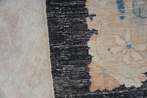 A black speckled border divides a pale woven texture from a patterned beige rug with muted floral accents.