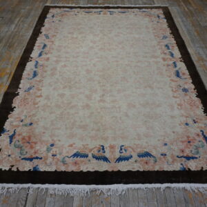 Pale rug featuring a pink floral field, a scalloped border, and deep blue accents on distressed wood flooring.