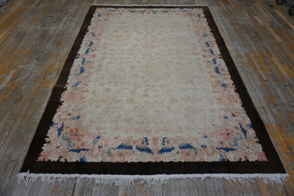 Pale rug featuring a pink floral field, a scalloped border, and deep blue accents on distressed wood flooring.