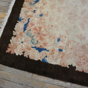 The rug features a scalloped dark brown border around a creamy field with pink and blue florals on wood flooring.
