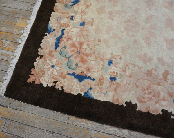 The rug features a scalloped dark brown border around a creamy field with pink and blue florals on wood flooring.
