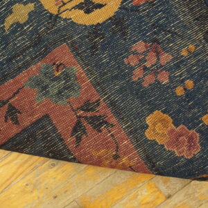 Blue rug with gold and burgundy floral patterns curled on worn plank wood flooring.