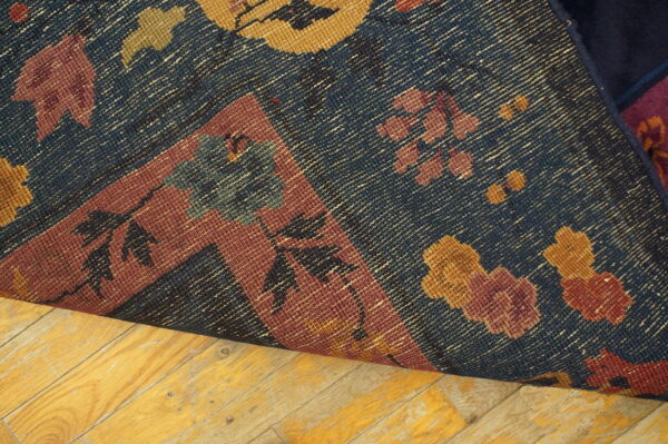 Blue rug with gold and burgundy floral patterns curled on worn plank wood flooring.