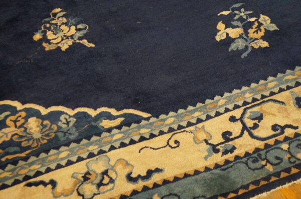 Navy blue rug detail with gold and teal floral medallions and a wide, intricately patterned border on wood floor.