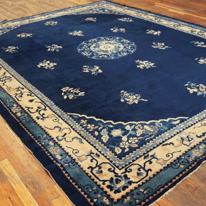 Deep blue rug featuring a beige and teal floral border and medallion, placed on polished wood floors.