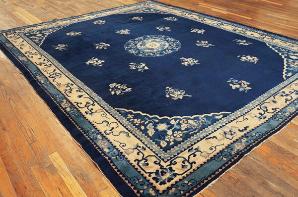 Deep blue rug featuring a beige and teal floral border and medallion, placed on polished wood floors.