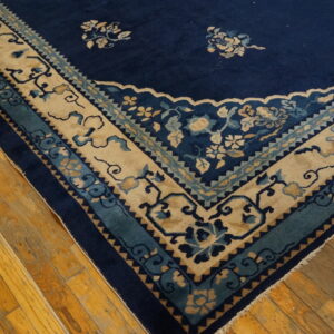 Navy blue rug corner with ornate beige, teal, and blue floral borders on distressed wood planks.