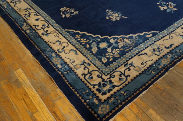 Navy blue rug corner with ornate beige, teal, and blue floral borders on distressed wood planks.