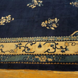 Navy rug with scattered tan floral field motifs and complex tan and teal patterned borders on wood.