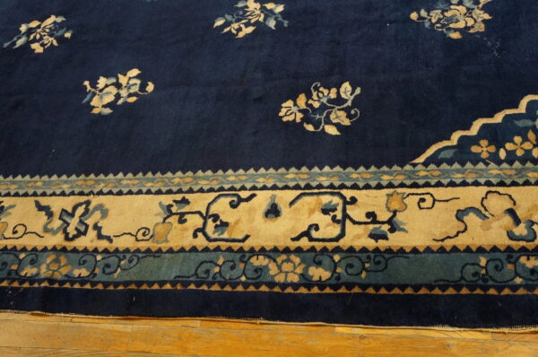 Navy rug with scattered tan floral field motifs and complex tan and teal patterned borders on wood.