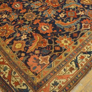 A corner view of a navy, rust, and cream patterned rug with stylized borders on light wood flooring.