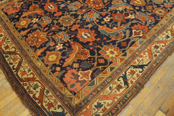 A corner view of a navy, rust, and cream patterned rug with stylized borders on light wood flooring.