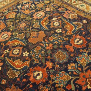 Low-pile rug with navy field and dense floral patterns in rust, coral, and teal colors on wood flooring.