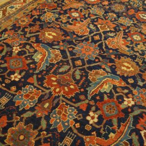 Navy and rust patterned rug featuring dense floral designs rests on natural wood plank flooring.