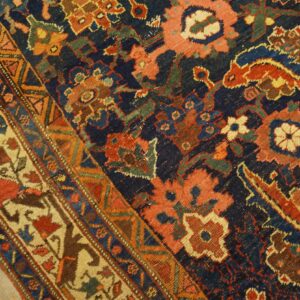 Intricate traditional rug pattern in navy, rust, and gold on textured low pile and wood flooring.