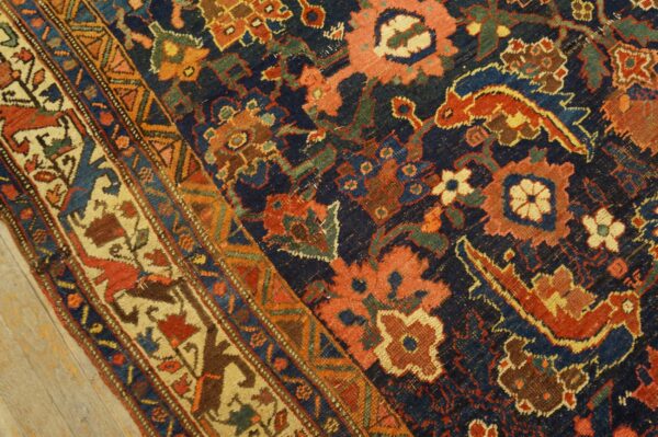 Intricate traditional rug pattern in navy, rust, and gold on textured low pile and wood flooring.