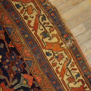 Detailed, low-pile rug border in navy, rust, and cream with animal motifs rests on distressed wooden planks.