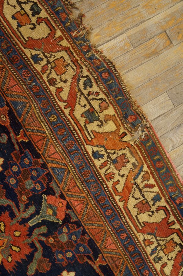 Detailed, low-pile rug border in navy, rust, and cream with animal motifs rests on distressed wooden planks.