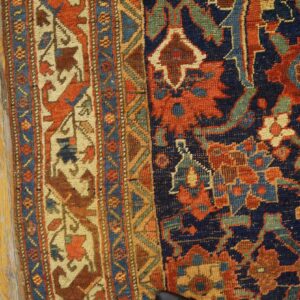 Detail of a traditional patterned rug with blue, rust, and cream colors on worn yellow wood.