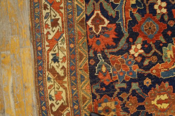 Detail of a traditional patterned rug with blue, rust, and cream colors on worn yellow wood.