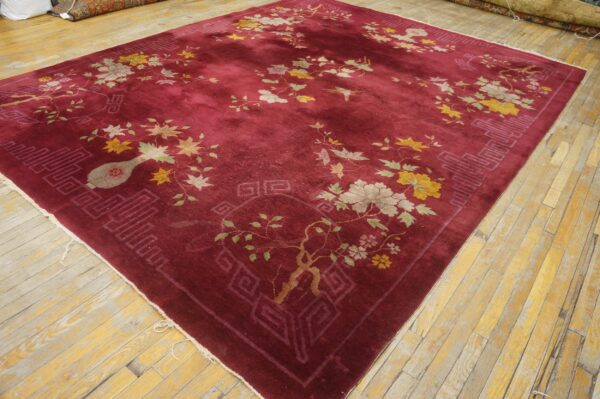 A deep red rug with scattered yellow, green, and cream floral designs on light wood planks.