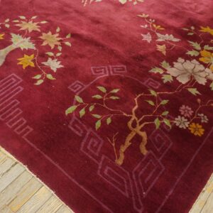 Burgundy rug with colorful botanical and geometric patterns rests on distressed wooden floorboards.