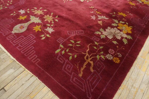 Burgundy rug with colorful botanical and geometric patterns rests on distressed wooden floorboards.