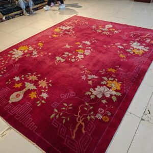 Large magenta area rug with yellow and cream floral vines and geometric borders on light tile floor.