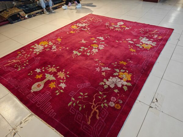 Large magenta area rug with yellow and cream floral vines and geometric borders on light tile floor.