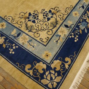 Ornate tan rug with navy and light blue floral borders rests on rustic wooden flooring.