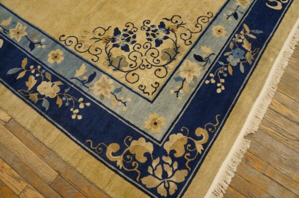 Ornate tan rug with navy and light blue floral borders rests on rustic wooden flooring.