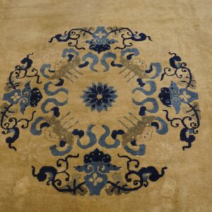 A tan rug featuring a central medallion pattern in dark blue, light blue, and gray.