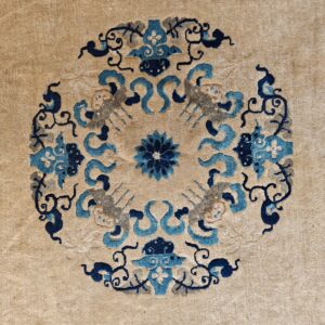 A tan rug displays a close-up circular medallion pattern featuring stylized motifs in blue, navy, and grey.