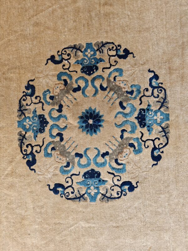 A tan rug displays a close-up circular medallion pattern featuring stylized motifs in blue, navy, and grey.