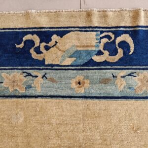Tan rug with thick indigo blue and light blue borders featuring stylized floral and scroll patterns.