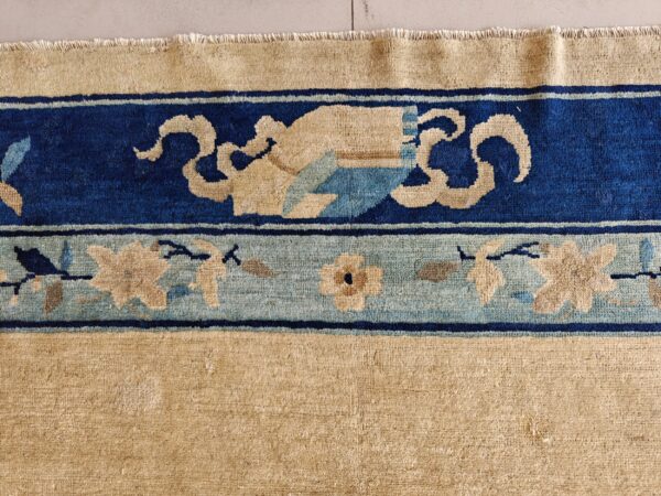 Tan rug with thick indigo blue and light blue borders featuring stylized floral and scroll patterns.