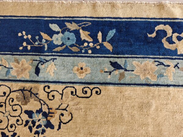 Tan high-pile rug with dark blue borders and light blue and beige scrolling floral designs.