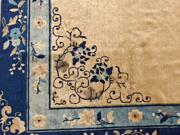 Detailed rug corner showing a beige field and dark blue, light blue, and tan floral borders.