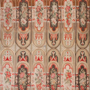 A flatweave rug features repeating vertical columns of arched architectural designs and floral bouquets in cream, brown, and red.