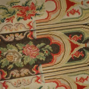 Flatweave rug with pink and red roses, green foliage, and striped background panels, resting on wood planks.