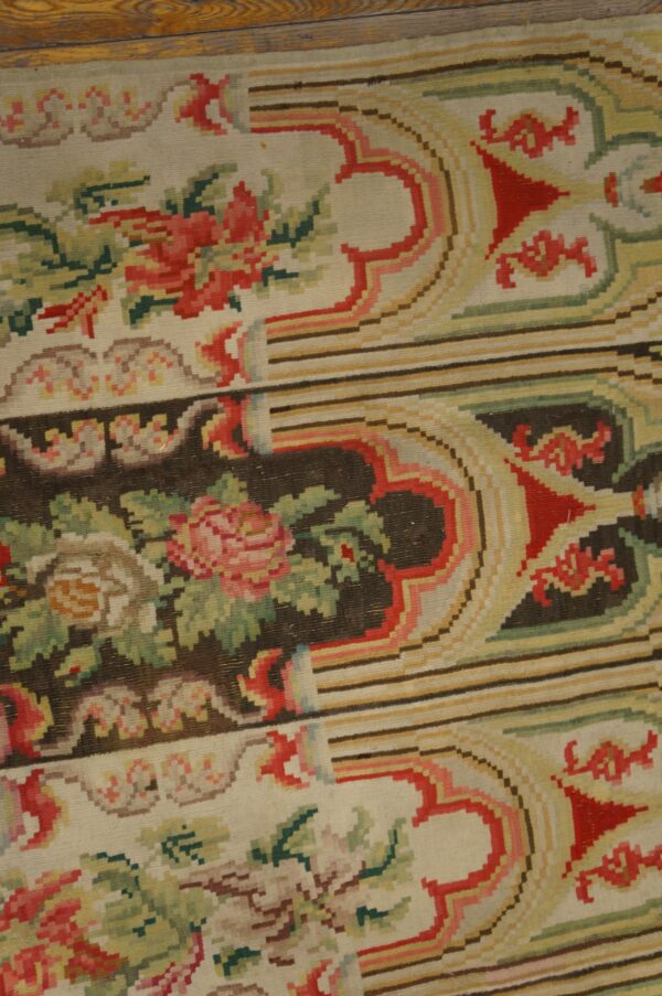 Flatweave rug with pink and red roses, green foliage, and striped background panels, resting on wood planks.