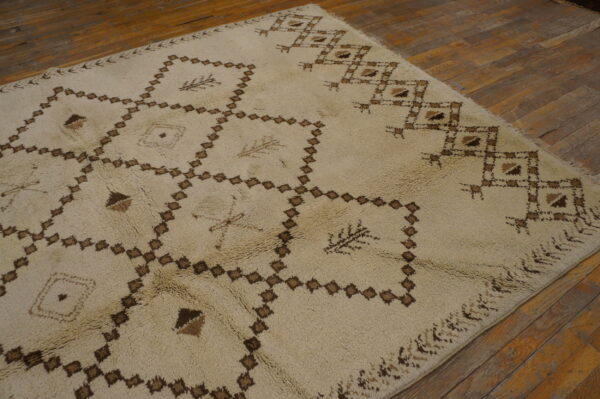 Shaggy cream rug featuring brown interlocking diamond patterns on distressed wood flooring.